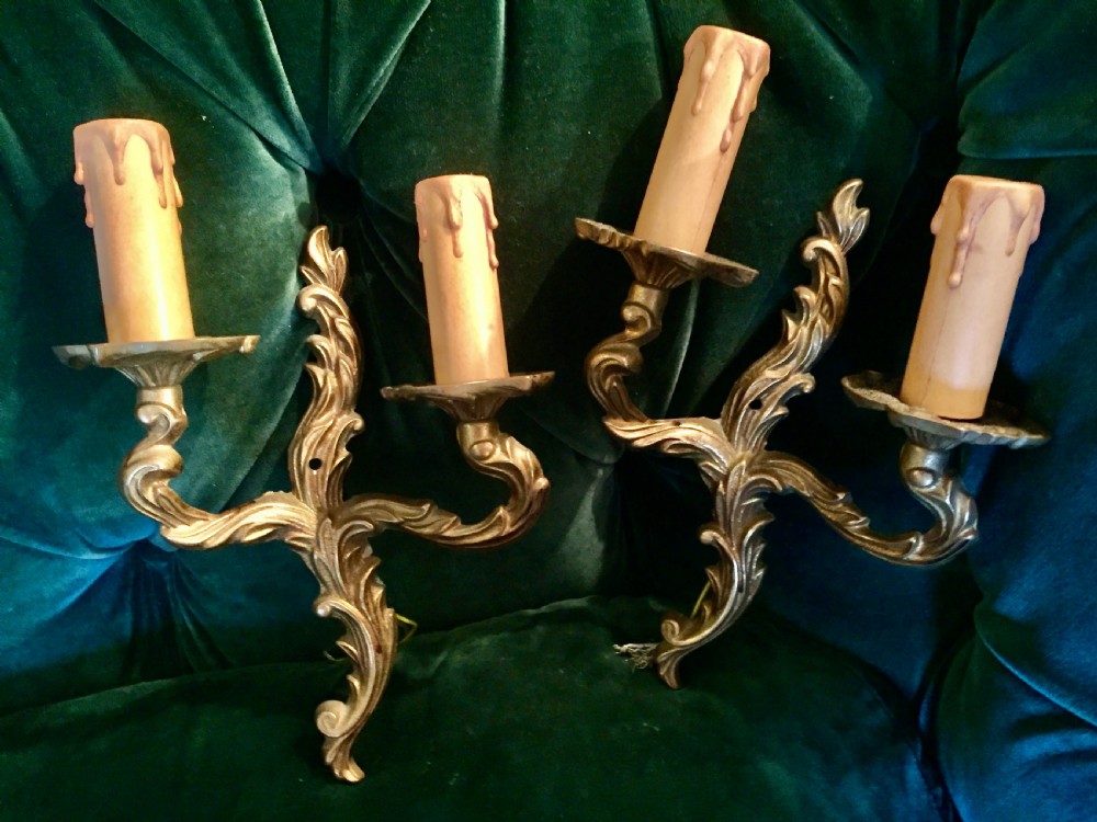 A pair of nineteenth-century French cast bronze two-arm wall sconces decorated with ornate leaf scrollwork and candle-effect sleeves.