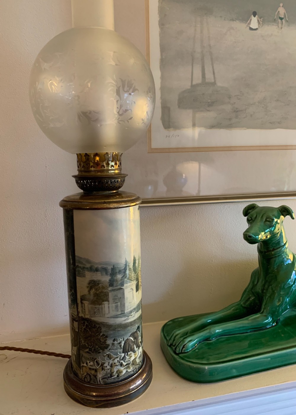 An antique French ceramic cylindrical oil lamp featuring a countryside hunt scene, brass gallery fittings, and a frosted glass globe shade.