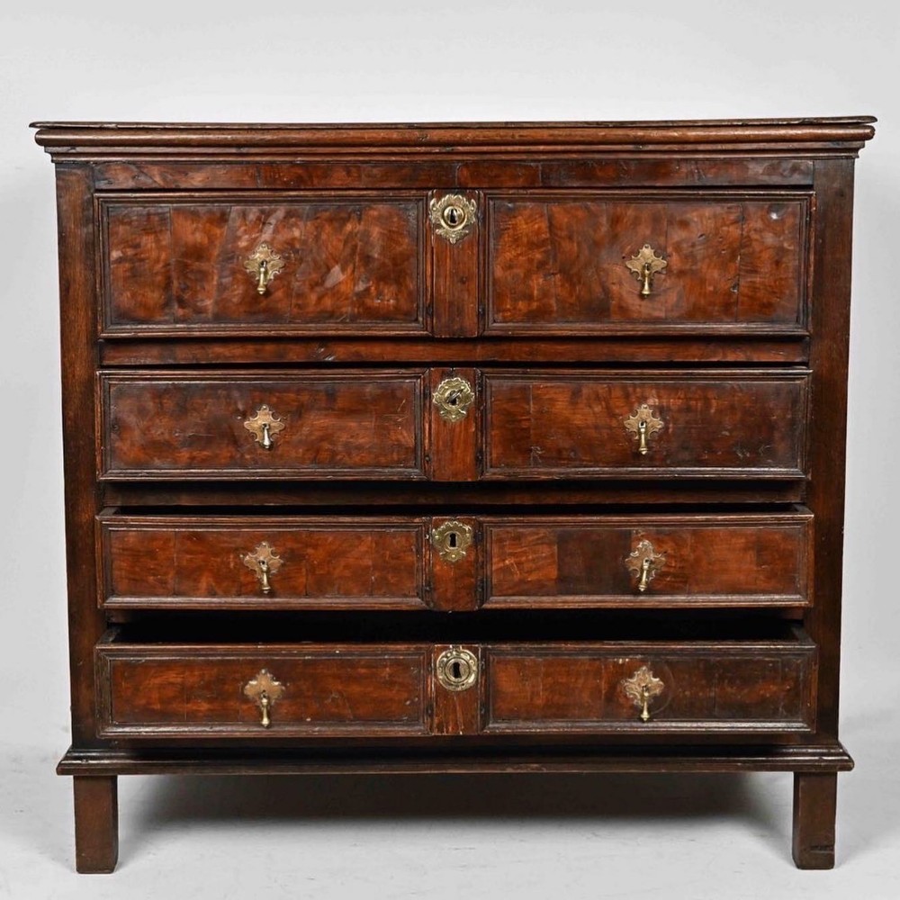 An antique oak-framed chest featuring four graduated walnut drawers fitted with brass teardrop handles and decorative escutcheons.