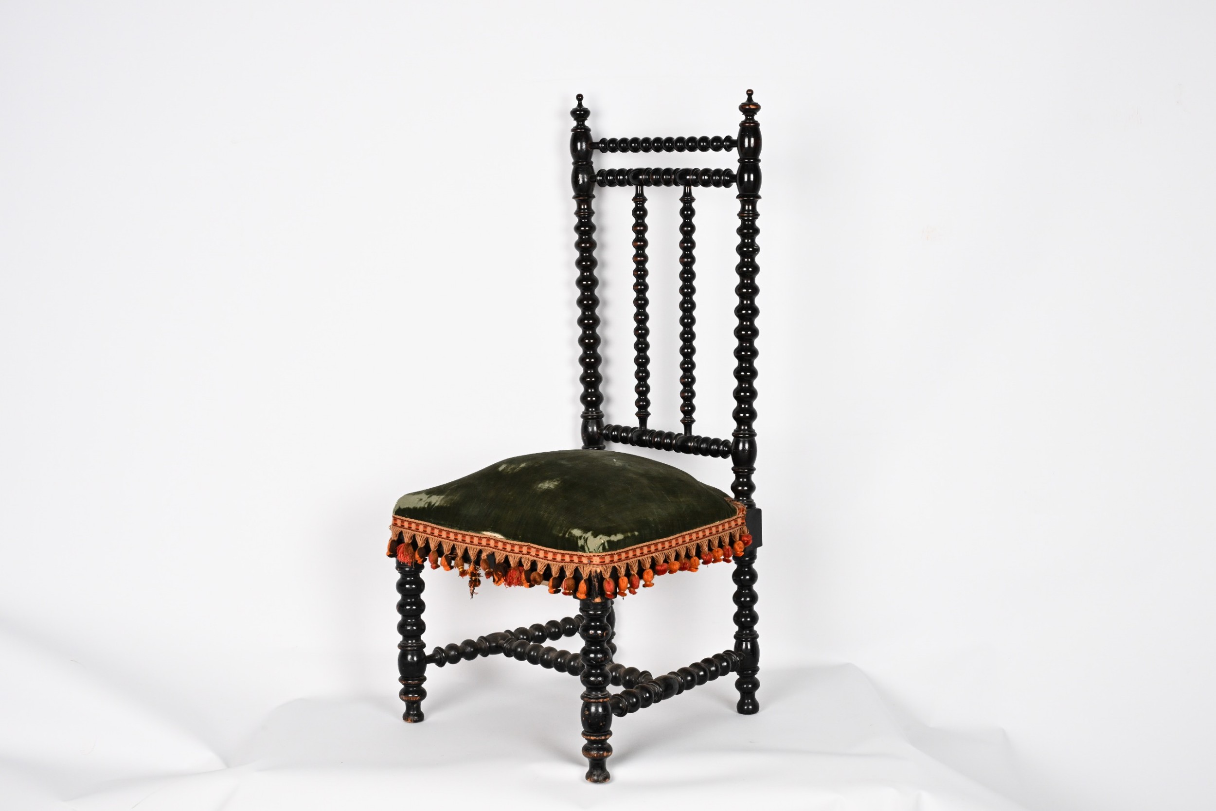 An ebonised wooden side chair featuring bobbin-turned legs and back spindles with a green velvet upholstered seat trimmed with tassel fringe.