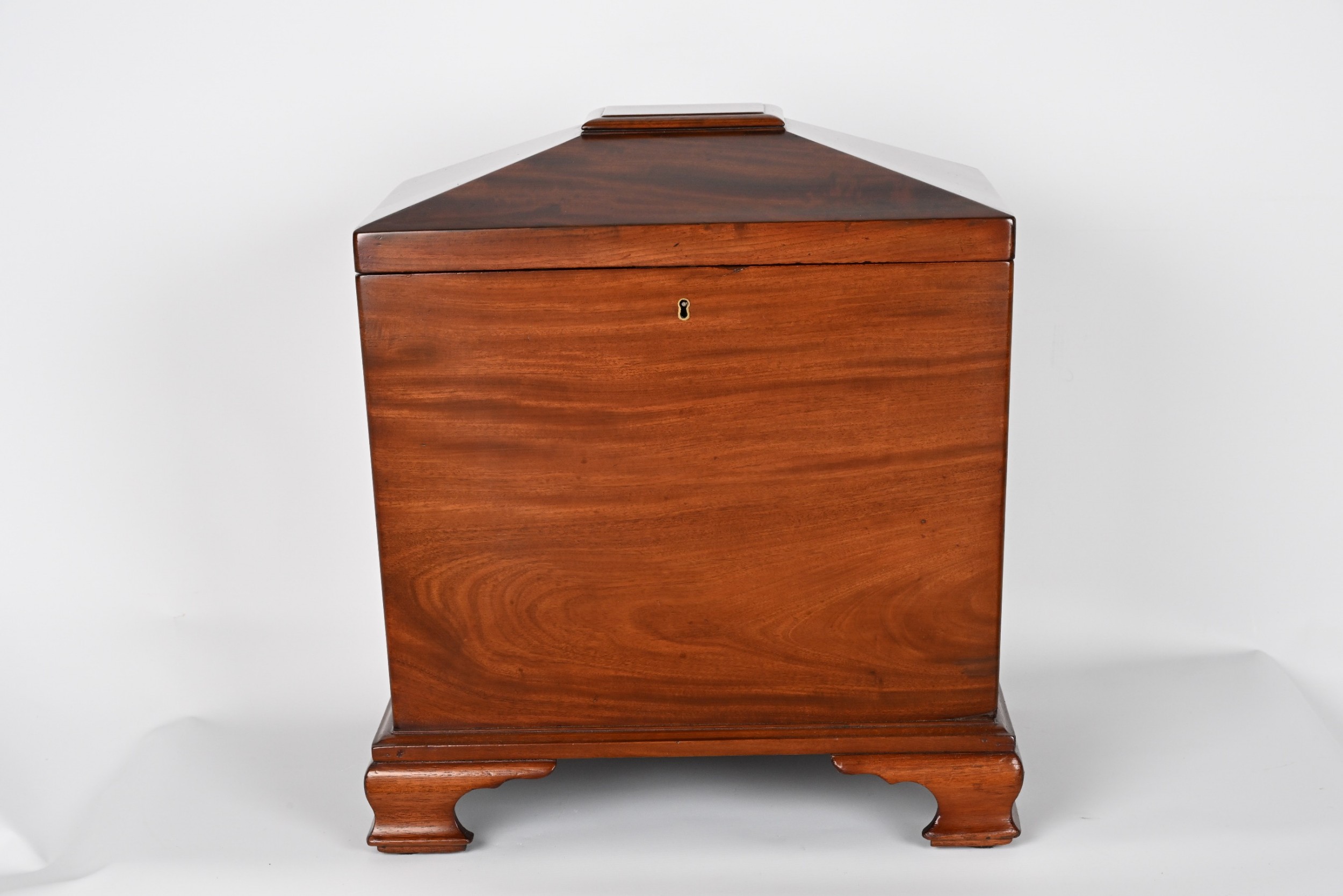 A George II mahogany cellarette featuring a hinged sarcophagus top, a brass keyhole escutcheon, and sculpted bracket feet.