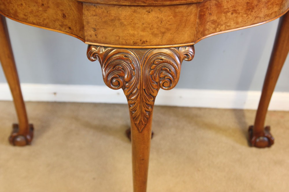 A demi-lune burr walnut fold-over card table featuring carved edges, cabriole legs, and carved ball-and-claw feet. View IV