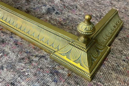 fig 2. An antique Victorian brass fireplace fender featuring a low rectangular kerb with decorative fluted moulding and detailed finials at each end.