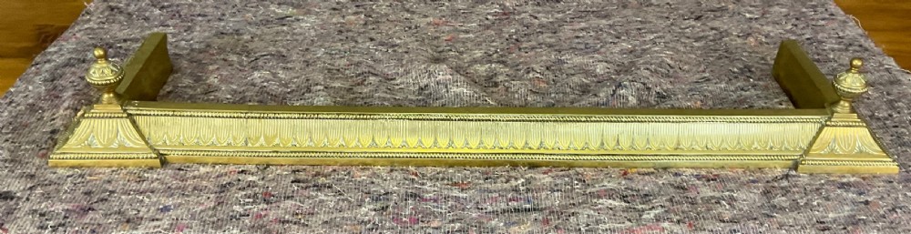 An antique Victorian brass fireplace fender featuring a low rectangular kerb with decorative fluted moulding and detailed finials at each end. View IV