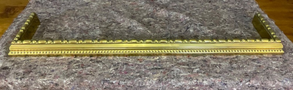 A low rectangular Victorian brass fireplace fender featuring raised beaded moulding and a polished golden finish. View II