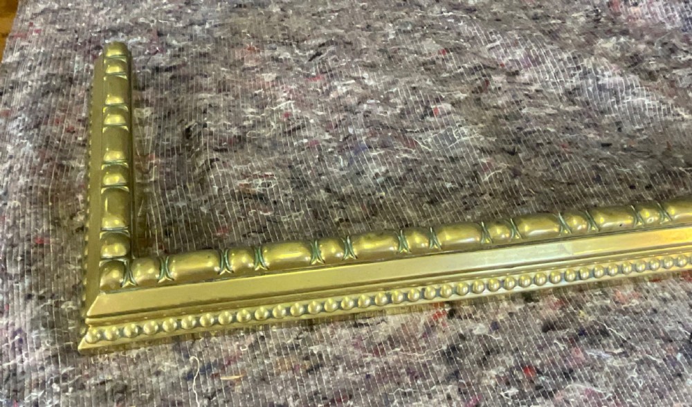 A low rectangular Victorian brass fireplace fender featuring raised beaded moulding and a polished golden finish. View III