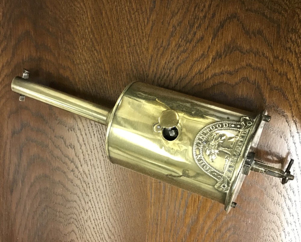 A cylindrical Georgian brass bottle spit jack featuring an embossed maker crest and a long top neck.