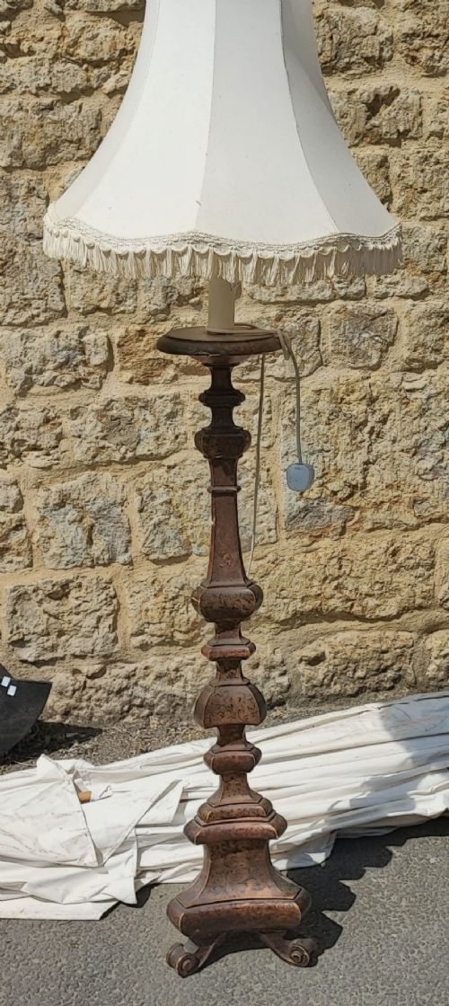 A dark carved wooden standard lamp featuring a baluster column and topped with a cream fabric lampshade trimmed with fringe. View V