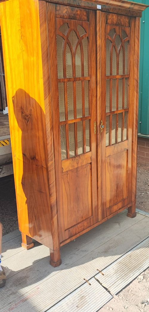 A tall 19th-century walnut display cabinet featuring two glazed doors with Gothic arched tracery above solid figured wood lower panels. View VII