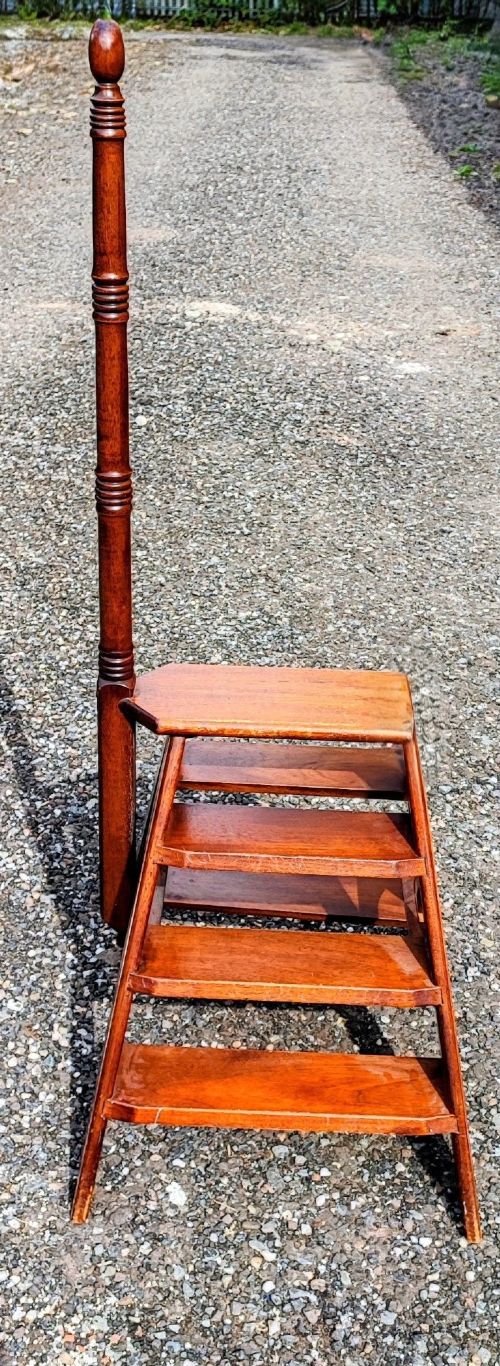 A set of wooden mahogany library steps featuring three treads, an A-frame support structure, and a tall turned wooden pole topped with a finial. View V