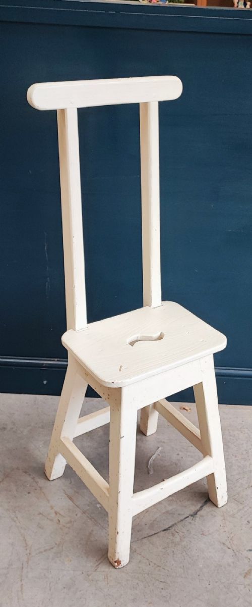 An off-white painted wooden step stool featuring a tall vertical back handle, splayed square legs, and a seat with a central carved handhole. View V