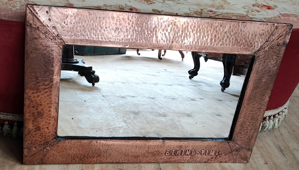 An antique art's and crafts Moto ( Behind Time) copper framed mirror.