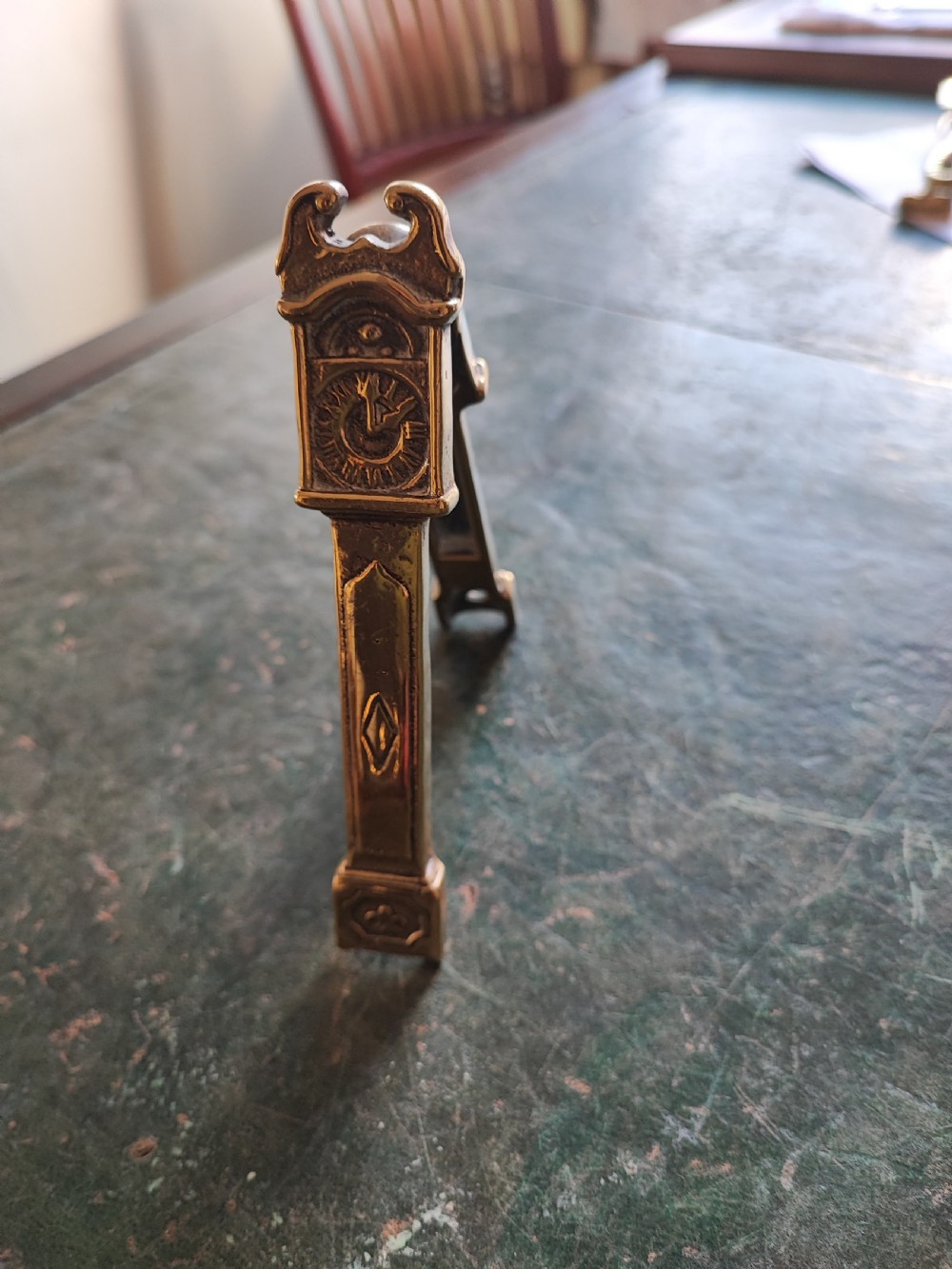 A small cast brass novelty door knocker shaped like a miniature grandfather clock with a detailed dial and pedestal base. View VII