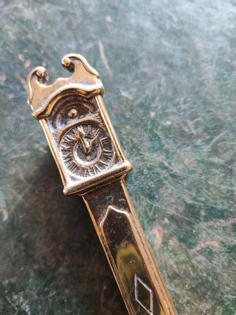 A small cast brass novelty door knocker shaped like a miniature grandfather clock with a detailed dial and pedestal base. View XI