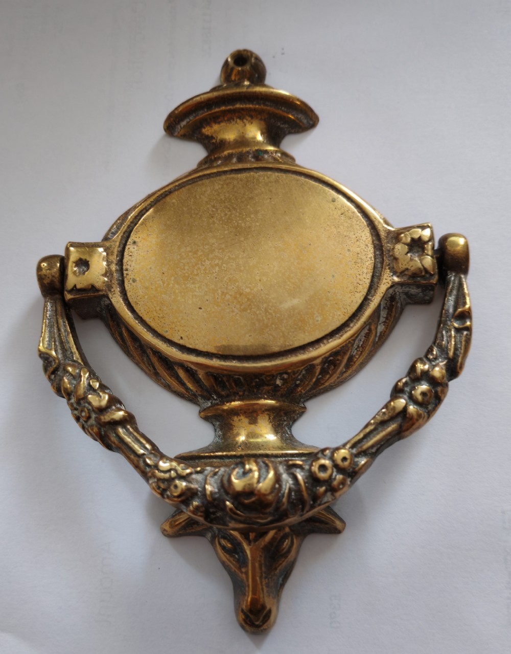A cast brass Neoclassical style door knocker shaped like an urn with a floral patterned hinged ring.