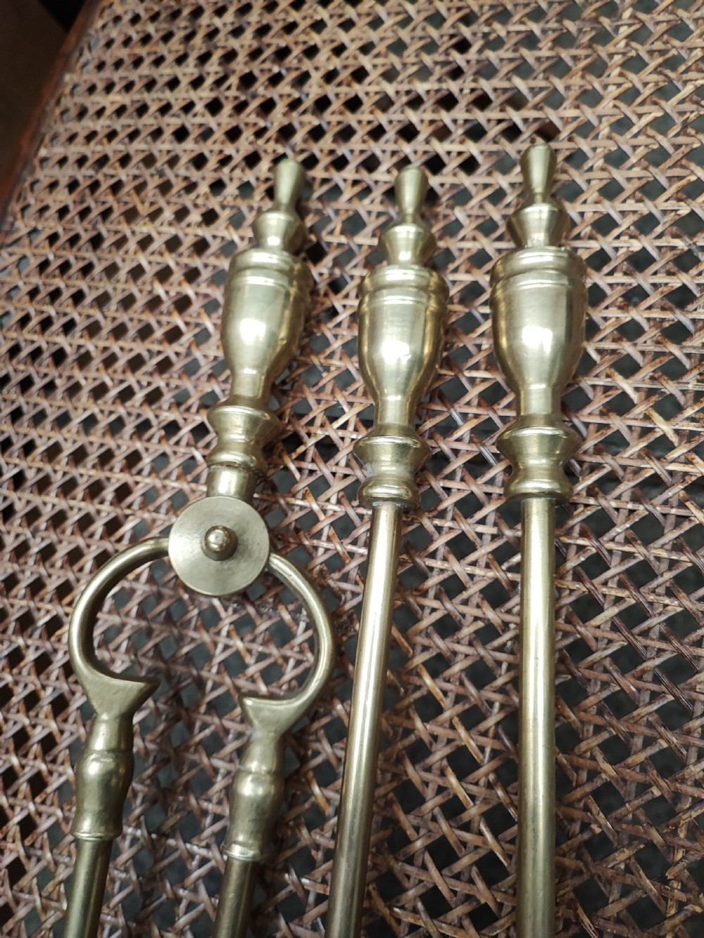 A set of three Victorian brass fire irons, including tongs, a shovel, and a poker with turned finial handles resting on a woven surface. View II