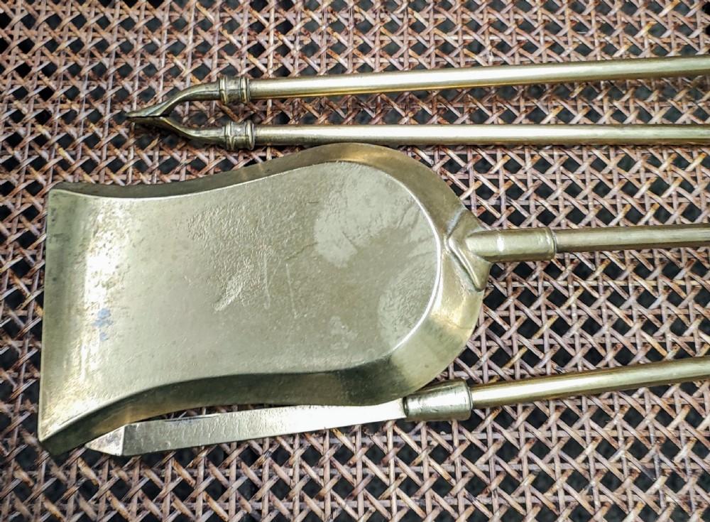 A set of three Victorian brass fire irons, including tongs, a shovel, and a poker with turned finial handles resting on a woven surface. View IV