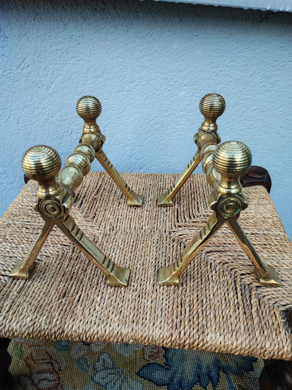 A pair of Arts and Crafts brass fire dogs featuring ribbed spherical finials and geometric angular legs.