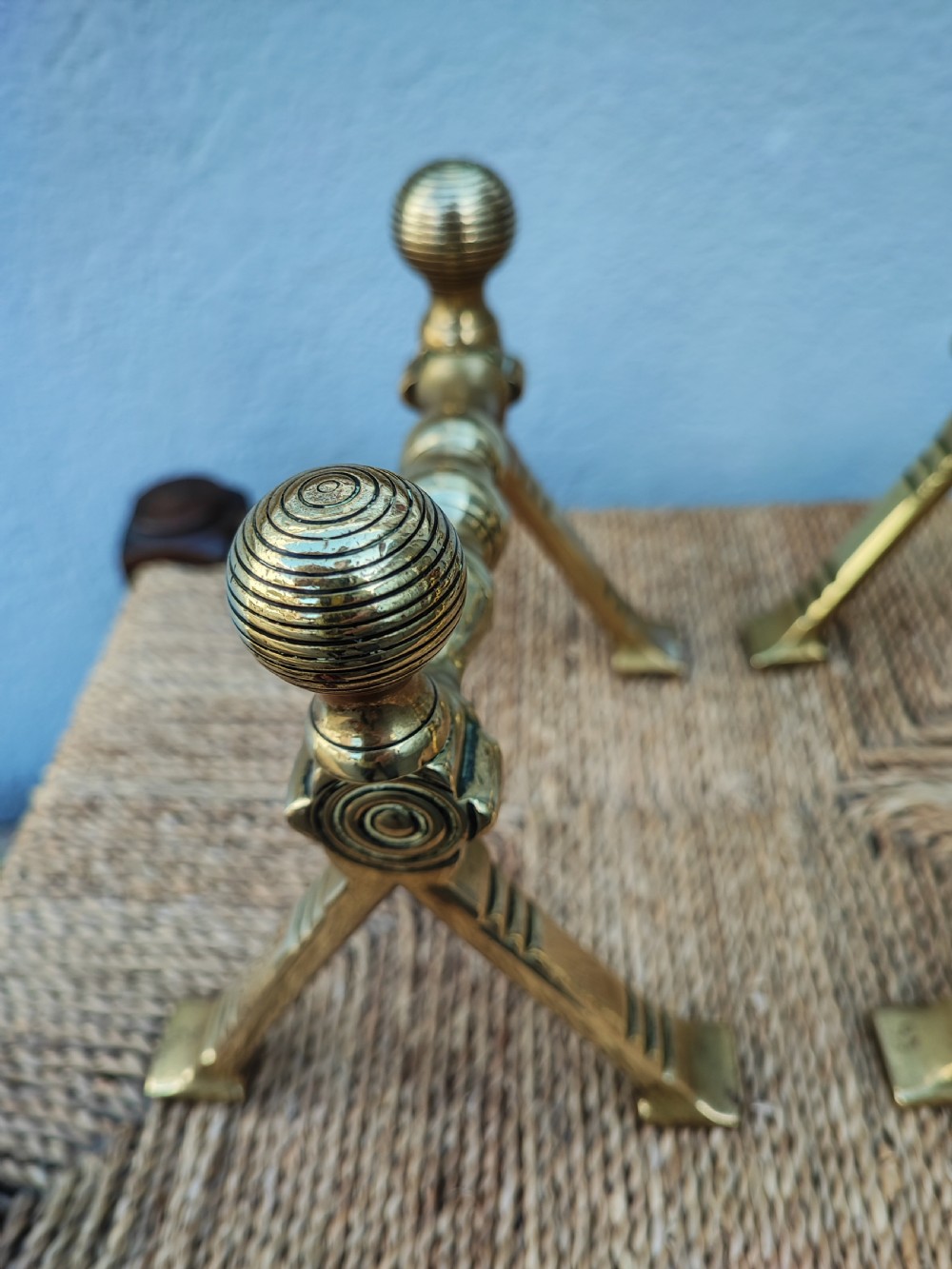 A pair of Arts and Crafts brass fire dogs featuring ribbed spherical finials and geometric angular legs. View II
