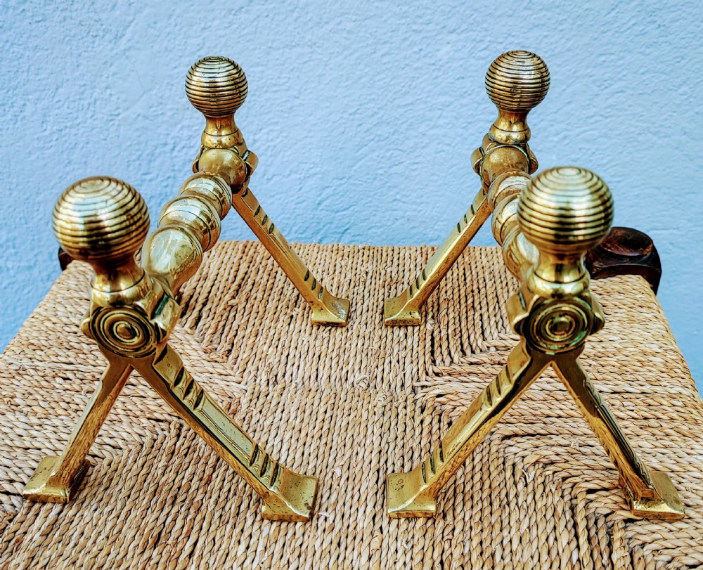 A pair of Arts and Crafts brass fire dogs featuring ribbed spherical finials and geometric angular legs. View IV