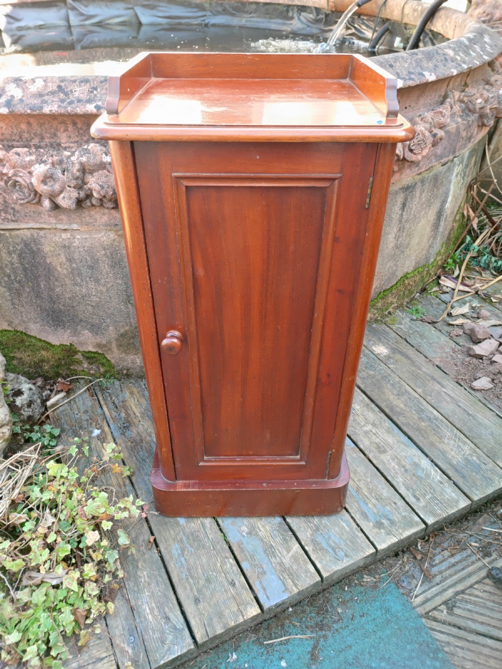 A tall Victorian mahogany bedside cabinet featuring a gallery top, a single recessed panel door with a wooden turned knob, and a solid plinth base.