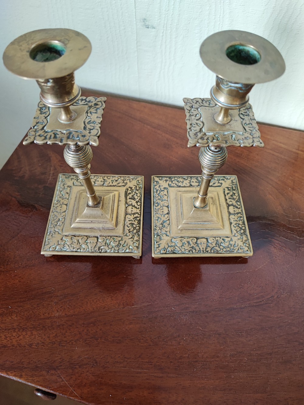 A matching pair of Victorian brass candlesticks featuring square relief bases, ribbed stems, square drip trays, and turned sconces. View II