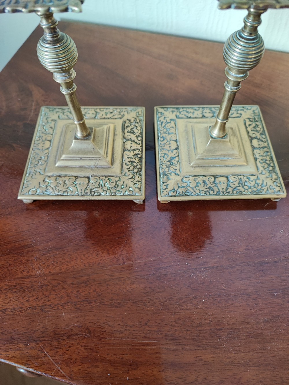 A matching pair of Victorian brass candlesticks featuring square relief bases, ribbed stems, square drip trays, and turned sconces. View IV