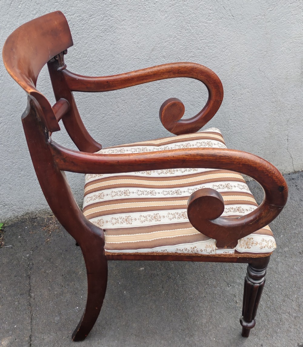 A Regency mahogany armchair with sweeping scroll armrests, a curved crest rail, turned front legs, and a striped upholstered seat.
