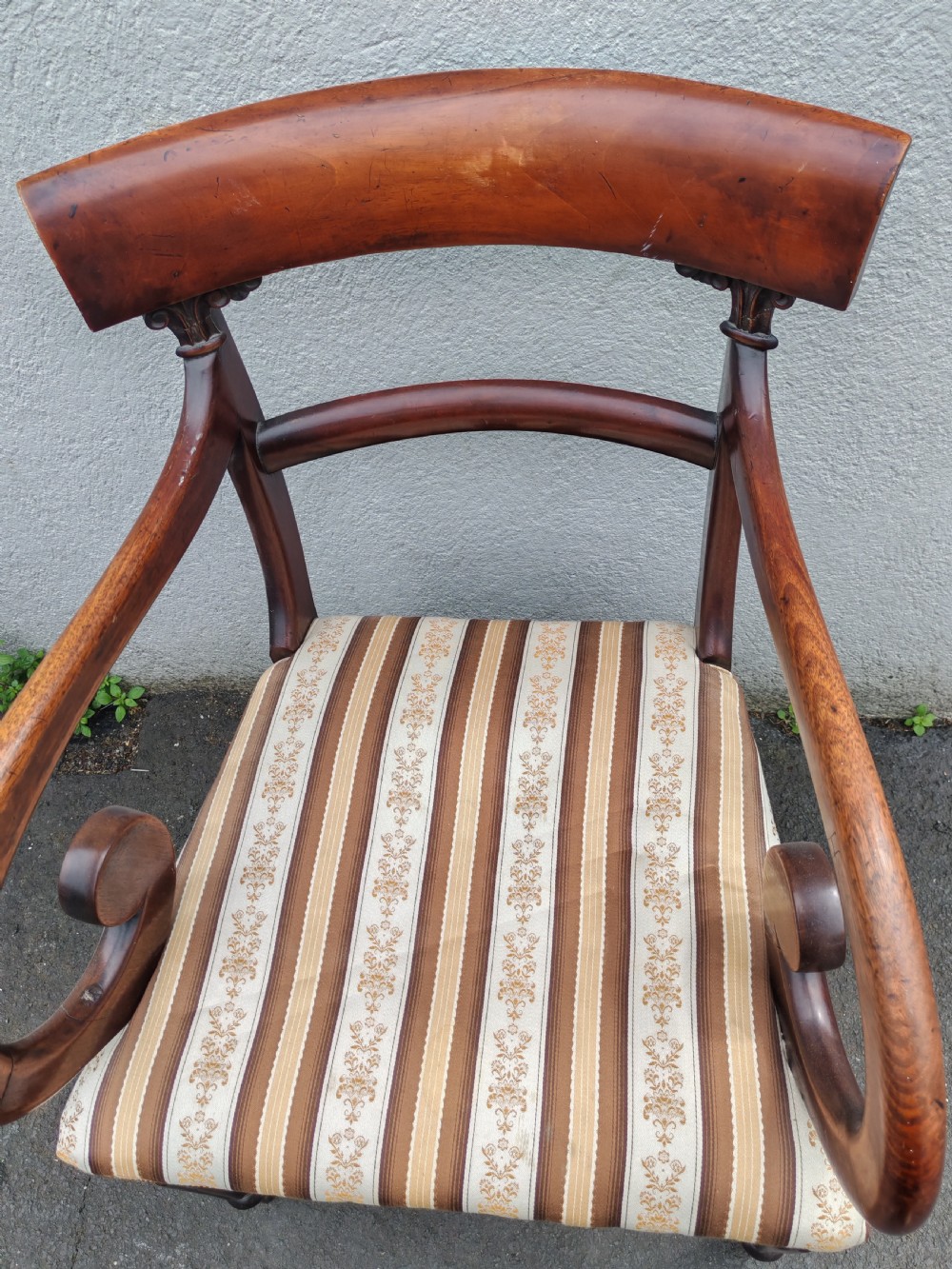 A Regency mahogany armchair with sweeping scroll armrests, a curved crest rail, turned front legs, and a striped upholstered seat. View II