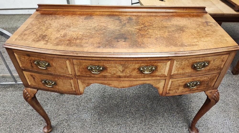 An antique golden burr walnut dressing table with five drawers, brass drop handles, and cabriole legs.