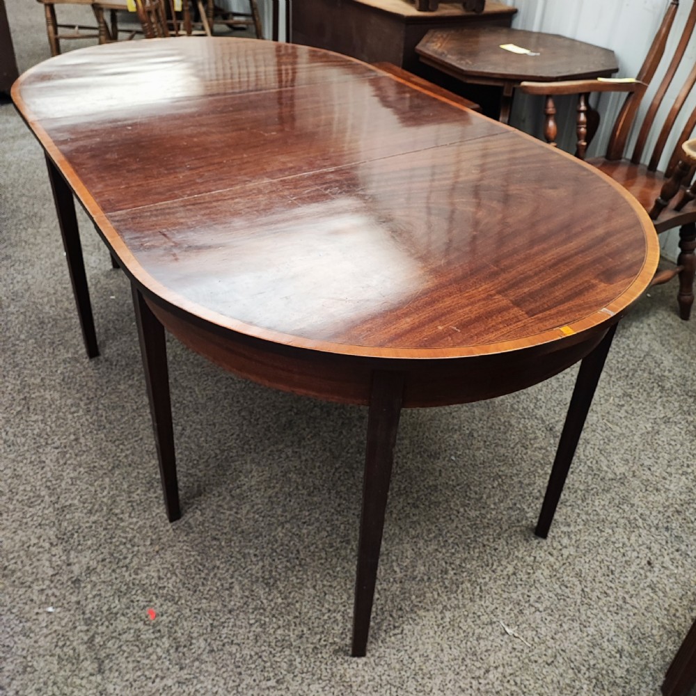 An oval Georgian style mahogany extendable dining table featuring a polished surface with crossbanded border detailing and four tapered square legs.