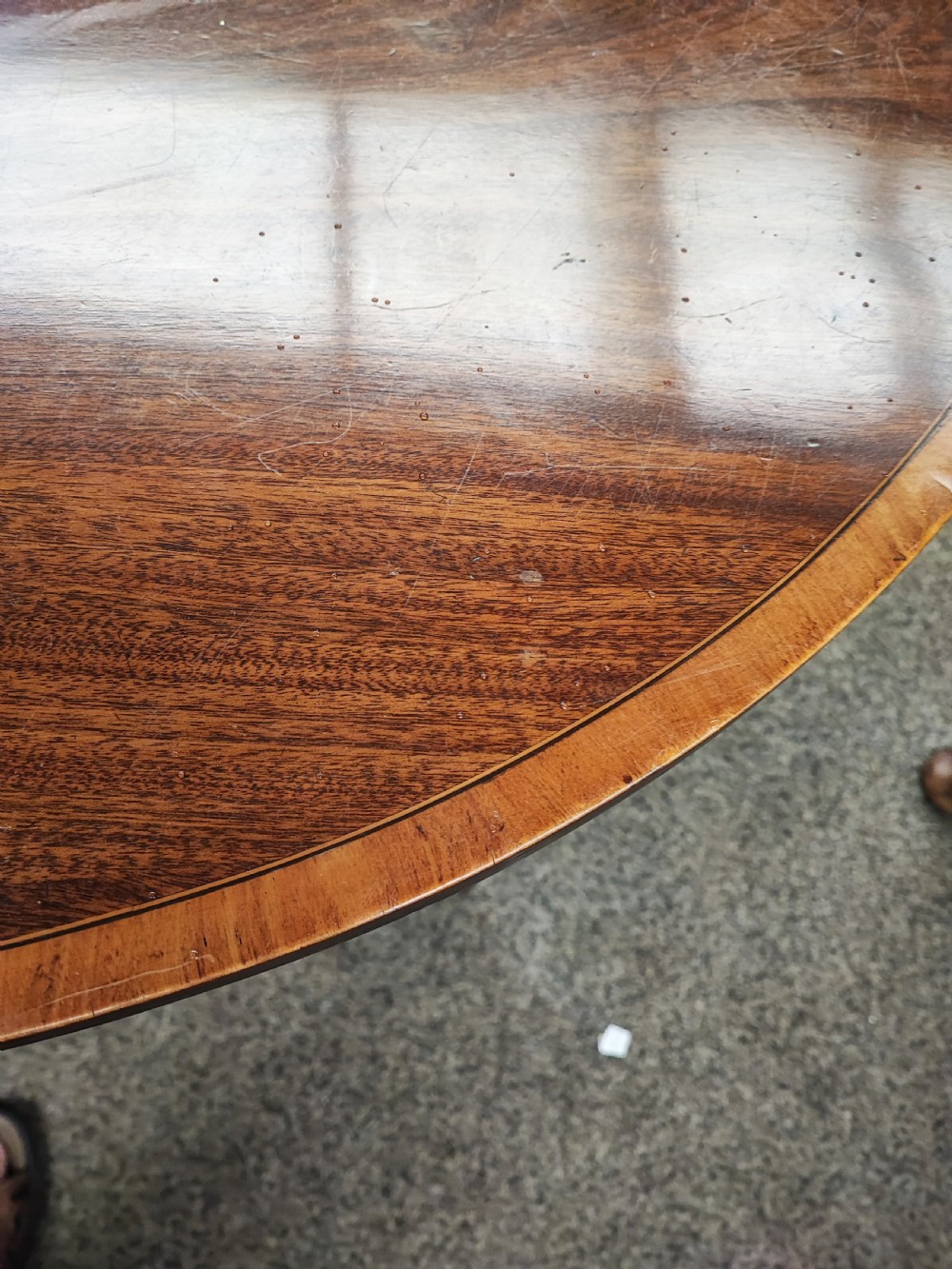 An oval Georgian style mahogany extendable dining table featuring a polished surface with crossbanded border detailing and four tapered square legs. View III