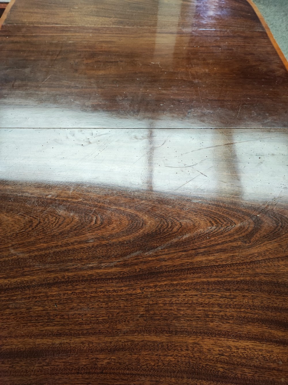 An oval Georgian style mahogany extendable dining table featuring a polished surface with crossbanded border detailing and four tapered square legs. View IV