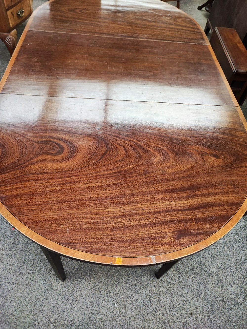 An oval Georgian style mahogany extendable dining table featuring a polished surface with crossbanded border detailing and four tapered square legs. View V