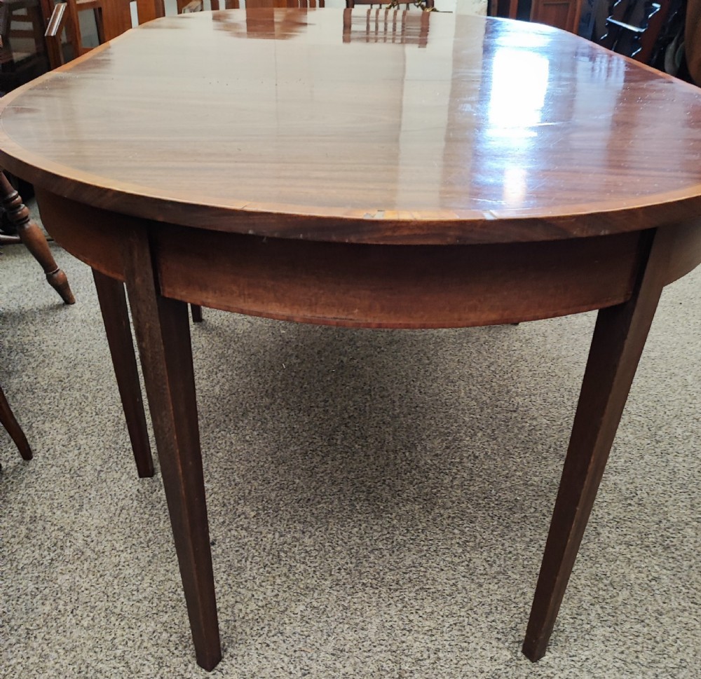 An oval Georgian style mahogany extendable dining table featuring a polished surface with crossbanded border detailing and four tapered square legs. View VIII