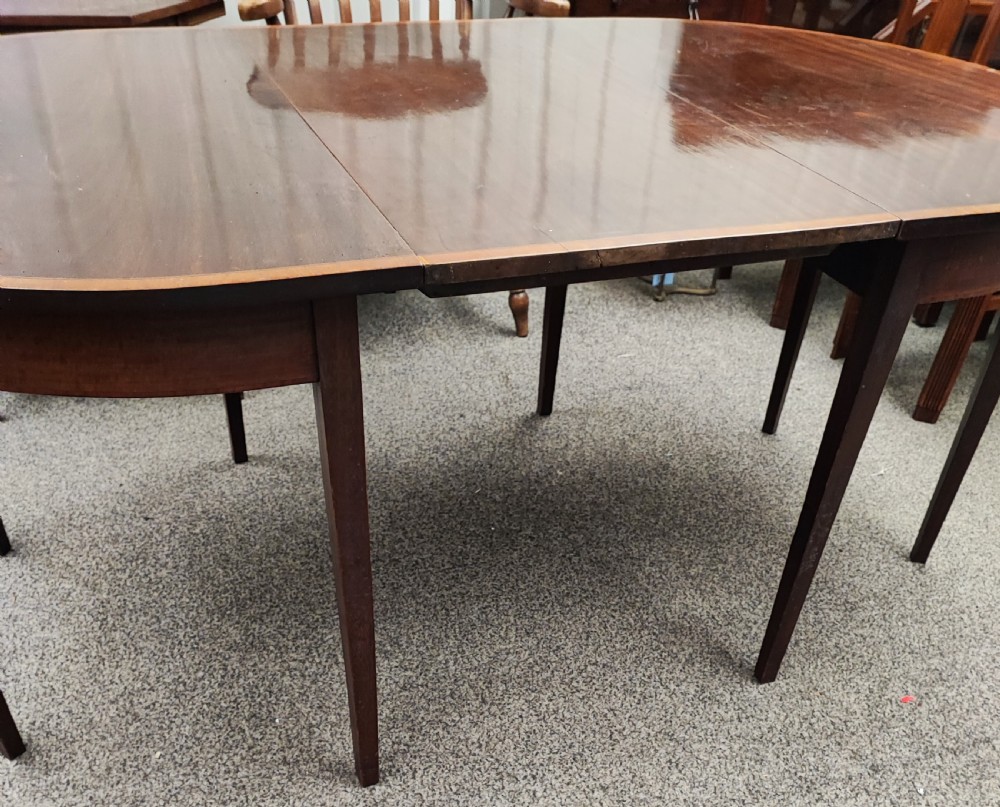An oval Georgian style mahogany extendable dining table featuring a polished surface with crossbanded border detailing and four tapered square legs. View X