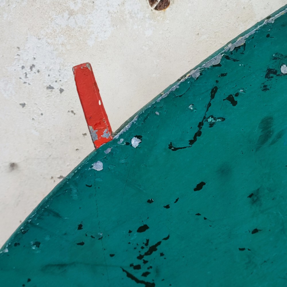 A circular white painted wooden wall sign featuring a raised relief motif of a sailboat with a green sail, red hull, and blue wave lines. View VI