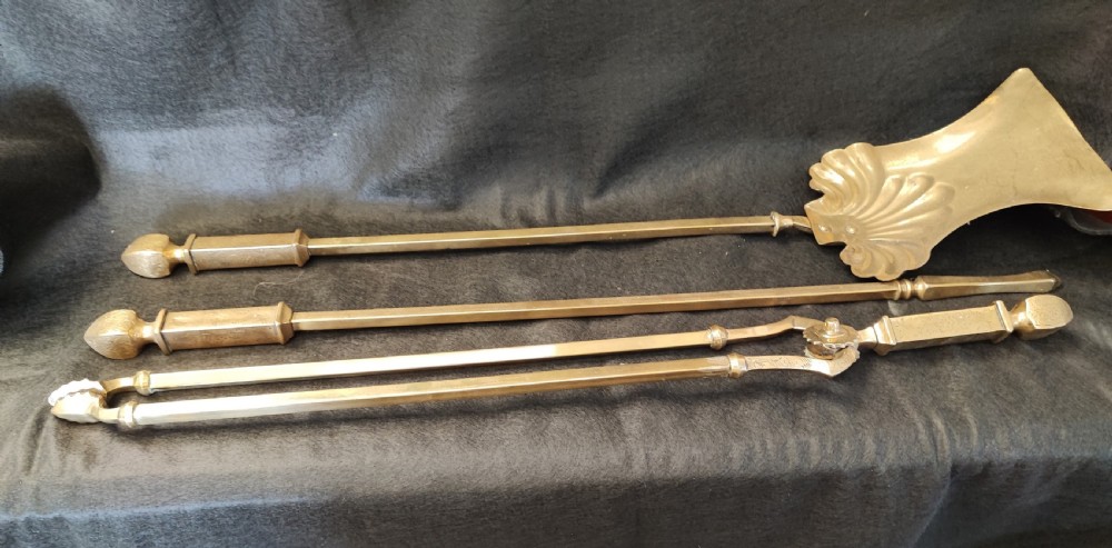 A set of three antique solid brass fire irons comprising a poker, tongs, and a shovel with a decorative shell pan.
