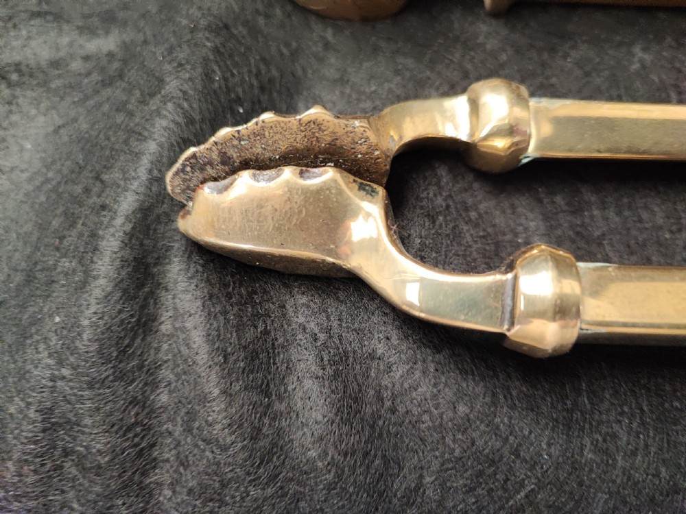 A set of three antique solid brass fire irons comprising a poker, tongs, and a shovel with a decorative shell pan. View II
