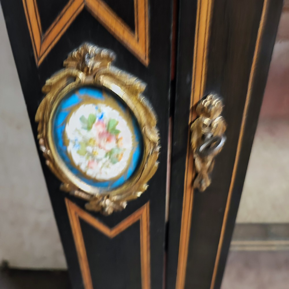 A black ebonised Victorian display cabinet featuring a central glazed door, gilt metal mounts, stringing inlay, and three porcelain plaques. View II
