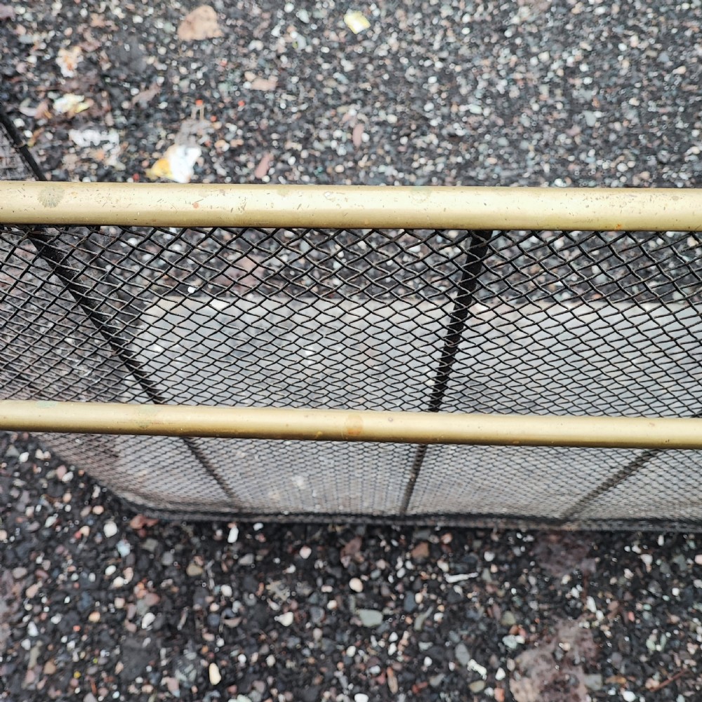 An antique nursery fireguard with a black woven wire mesh body, curved sides, and an upper tubular brass rail. View II
