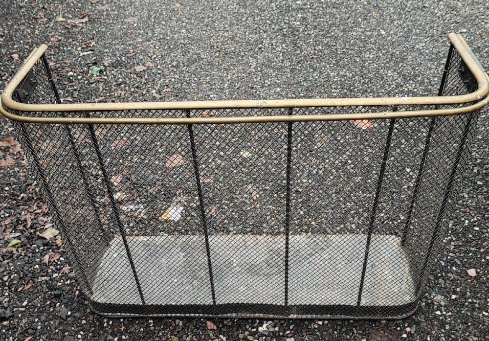 An antique nursery fireguard with a black woven wire mesh body, curved sides, and an upper tubular brass rail. View X