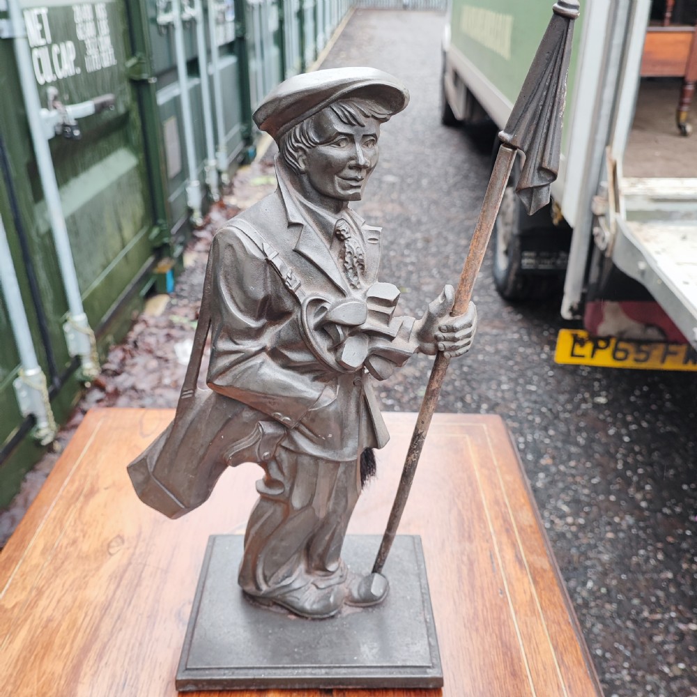 A dark cast metal companion set stand depicting a golfer caddy holding a flag pole and carrying a golf bag on a rectangular base.