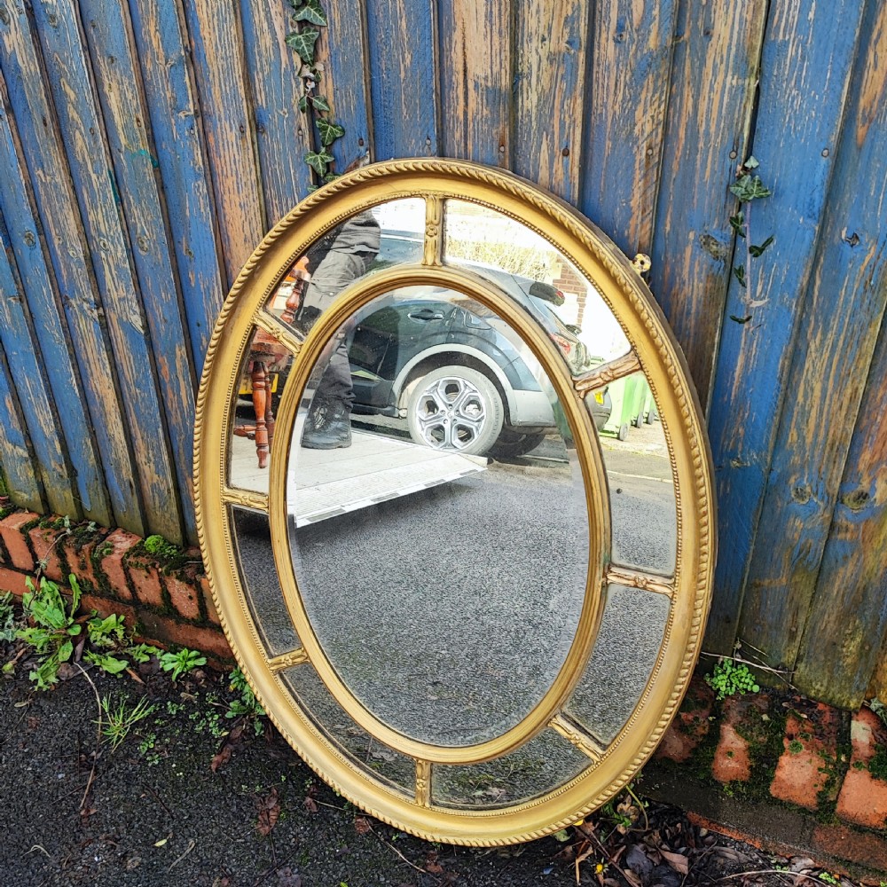 A large gold gilt oval wall mirror featuring a rope twist outer moulding and segmented glass border surrounding an inner oval mirror pane. View II