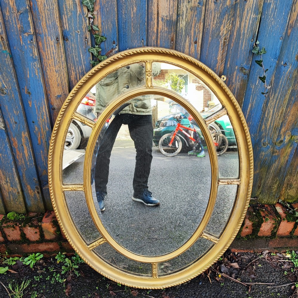 A large gold gilt oval wall mirror featuring a rope twist outer moulding and segmented glass border surrounding an inner oval mirror pane. View V