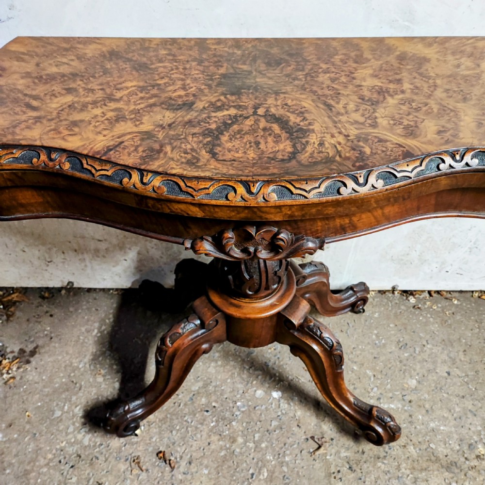 Victorian burr walnut fold-over card table featuring a serpentine top with carved apron details, supported by a central carved pedestal on four scroll-foot legs. View III