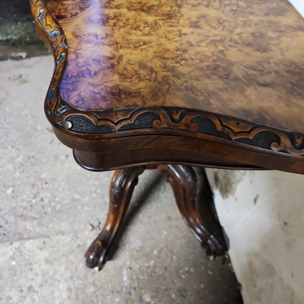 Victorian burr walnut fold-over card table featuring a serpentine top with carved apron details, supported by a central carved pedestal on four scroll-foot legs. View V