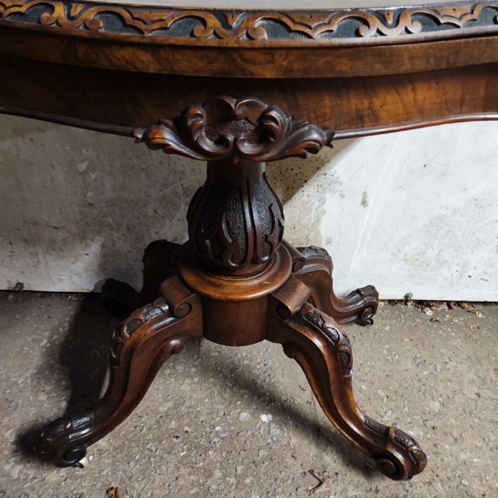 Victorian burr walnut fold-over card table featuring a serpentine top with carved apron details, supported by a central carved pedestal on four scroll-foot legs. View IX