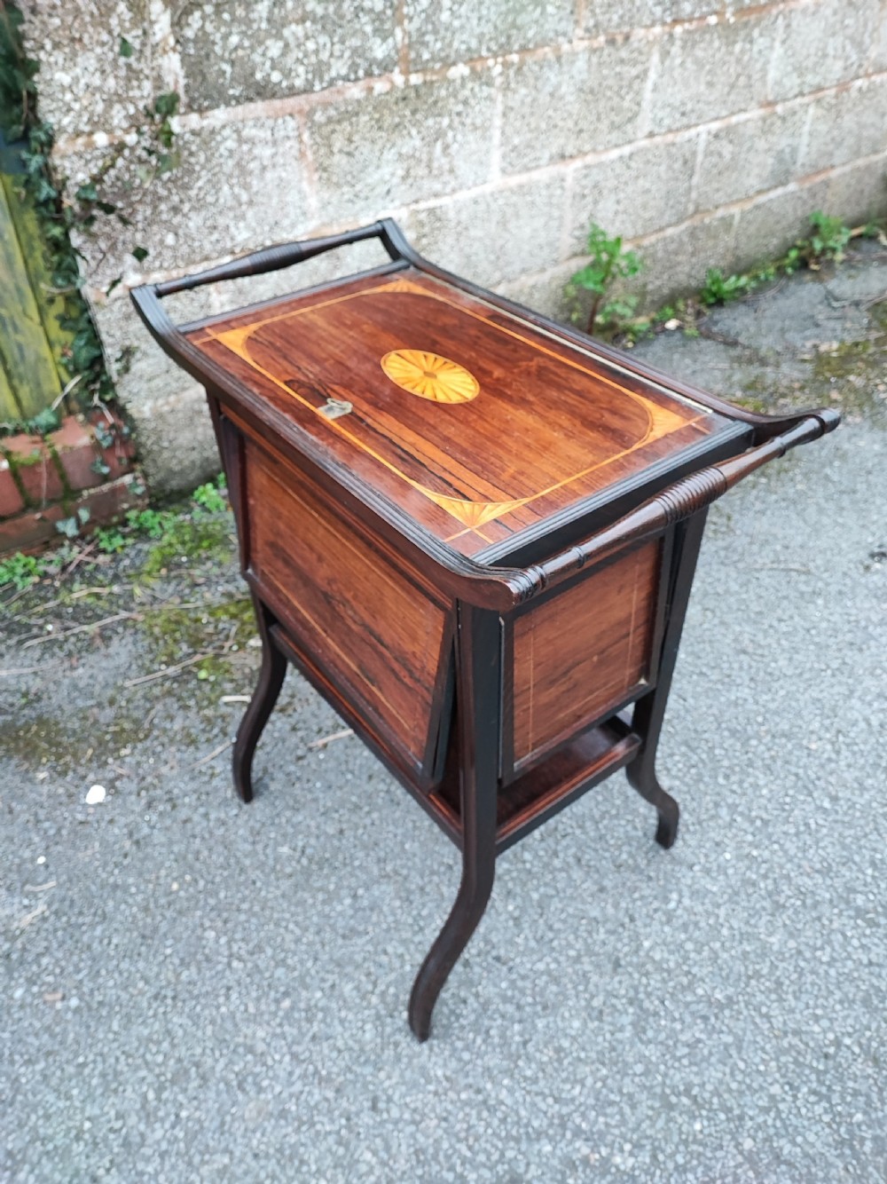 An antique rosewood work table featuring top marquetry inlay with a central sunburst motif, turned side handles, a lower shelf, and curved legs.