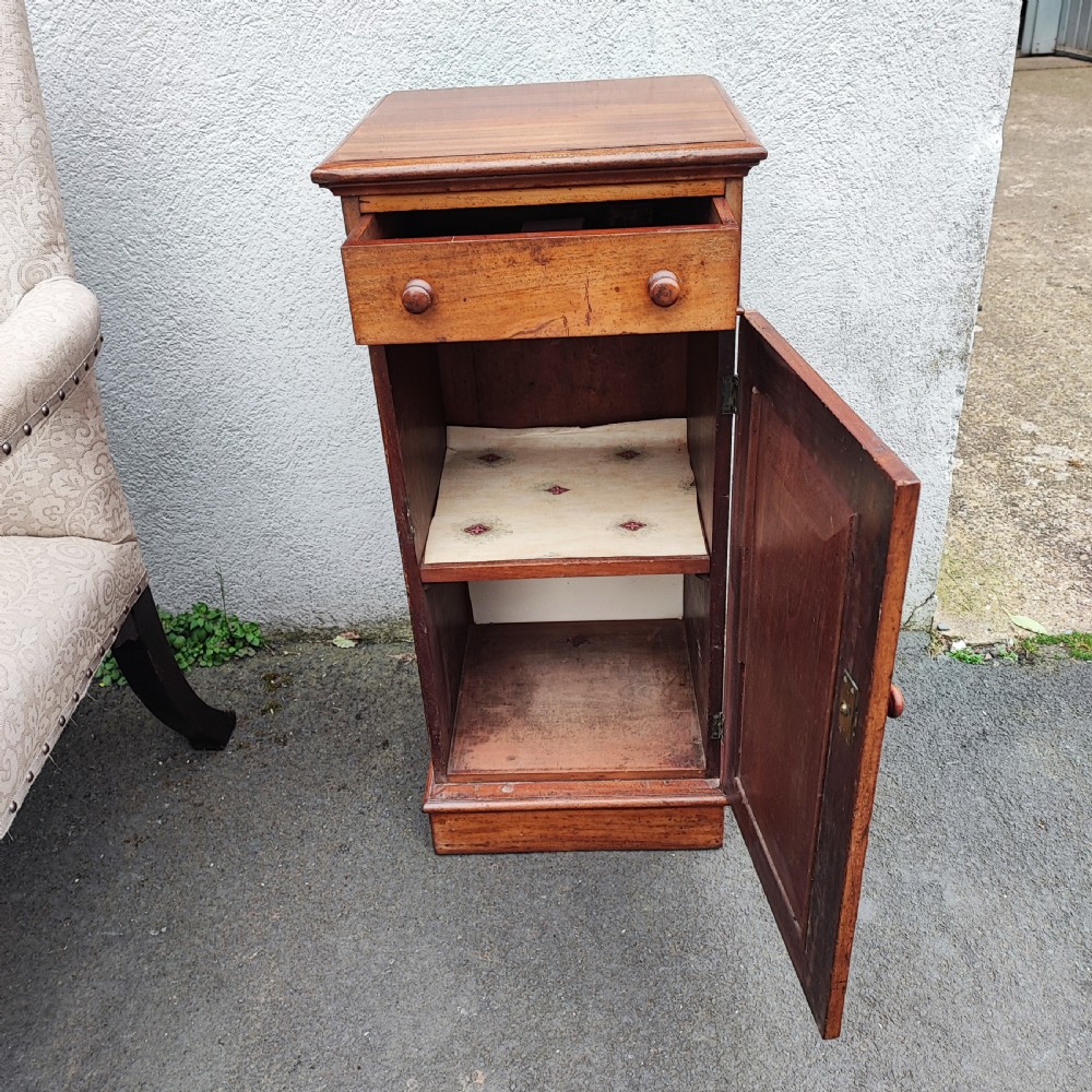 A tall, narrow mahogany pedestal bedside cabinet featuring a top drawer with turned wooden knobs above a single panelled cupboard door resting on a solid plinth base. View V